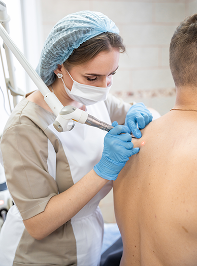 Clinician performing a minor skin procedure with a dermal device on a patient’s back at Windmill Practice.